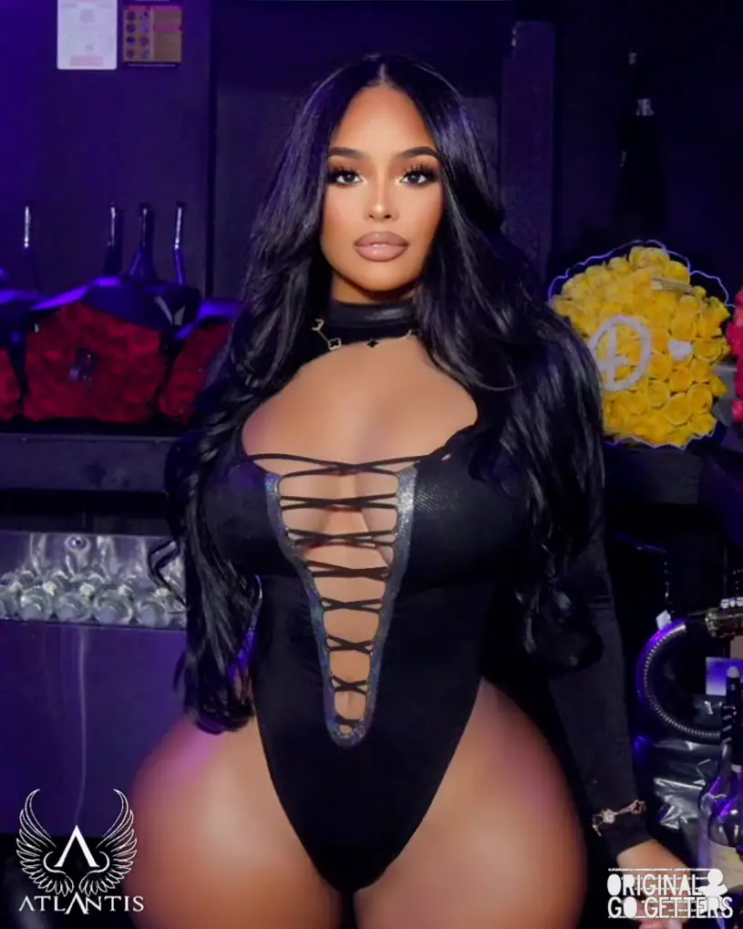 A woman with long black hair in a black, lace-up bodysuit poses in a dimly lit room. Branded Atlantis and Original Go Getters logos appear, evoking the vibrant nightlife of strip club Jamaica, with yellow and red flower arrangements in the background.